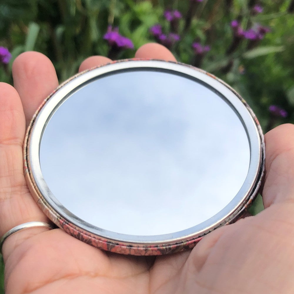 The mirrored side of the pocket mirror. The mirror fills the entire back, except for a small silver border.