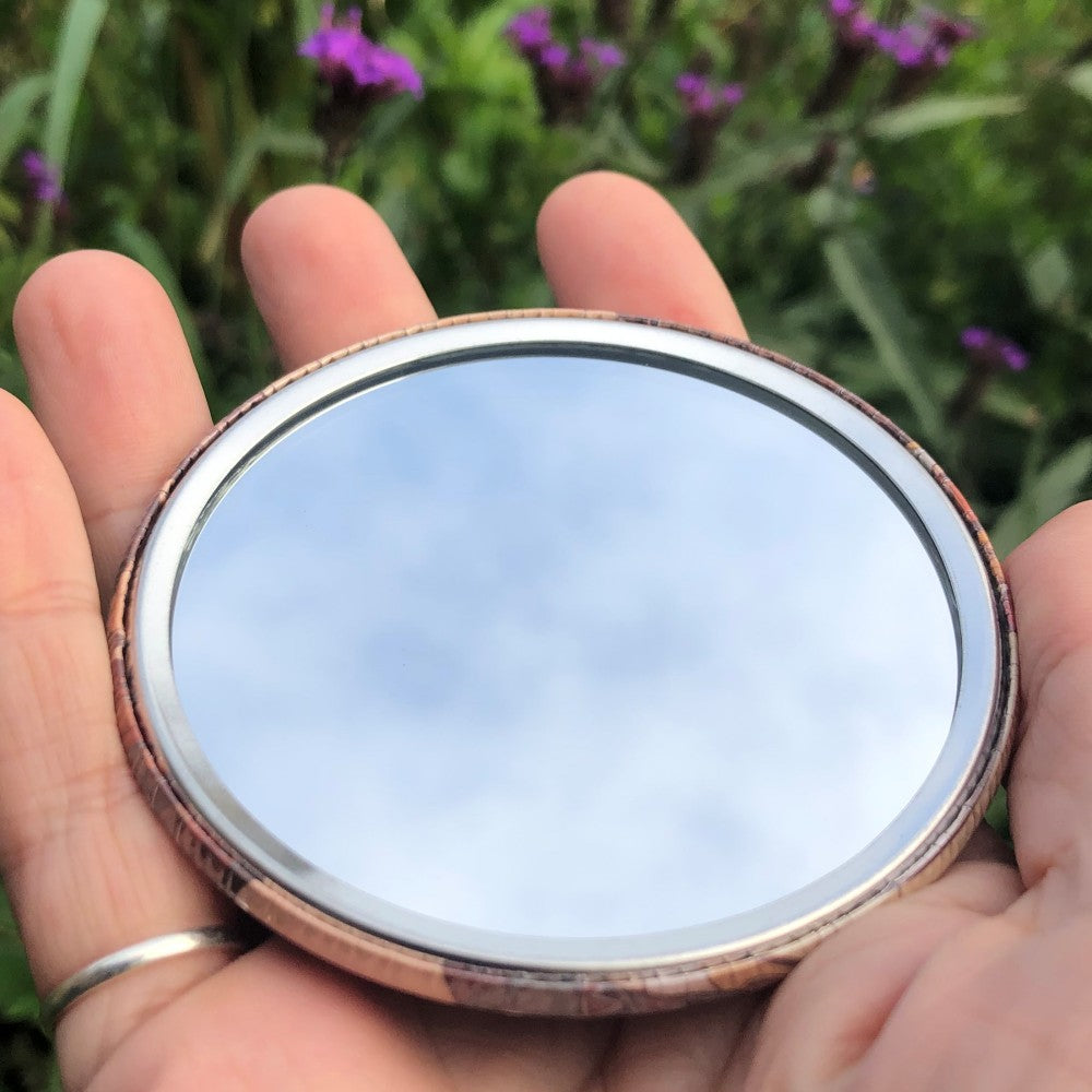 The mirrored side of the pocket mirror. The mirror fills the entire back, except for a small silver border.