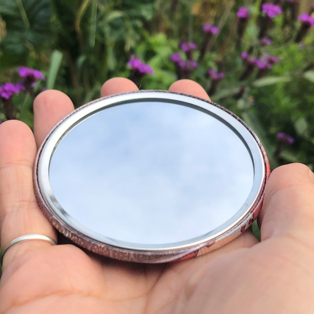 The mirrored side of the pocket mirror. The mirror fills the entire back, except for a small silver border.