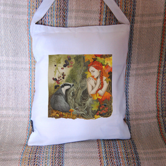 A woodland scene. On the left is a badger, sitting against a moss-covered tree trunk in the centre of the image, looking towards a crouching woman with bright red hair, her bare arms folded across her chest with her hands over her shoulders. She looks towards the badger with eyes part-closed. Blackberries hang above the badger, with autumn leaves and mushrooms at its feet. The woman is surrounded by large, autumn coloured leaves, with blackberries at her knees. Overall colours are oranges, reds and greens.