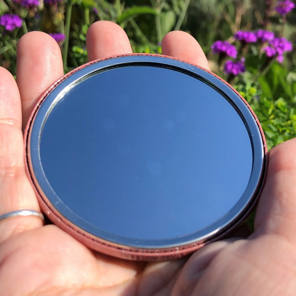 The mirrored side of the pocket mirror. The mirror fills the entire back, except for a small silver border.