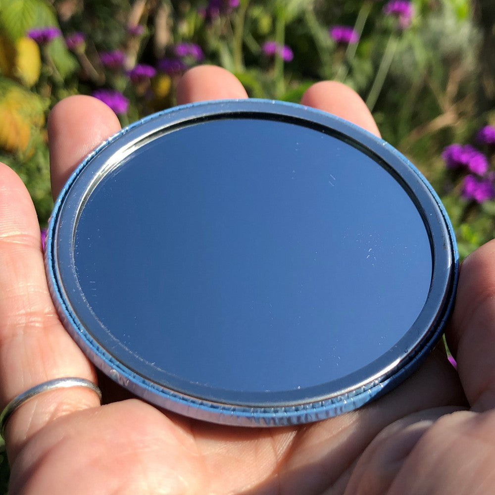 The mirrored side of the pocket mirror. The mirror fills the entire back, except for a small silver border.