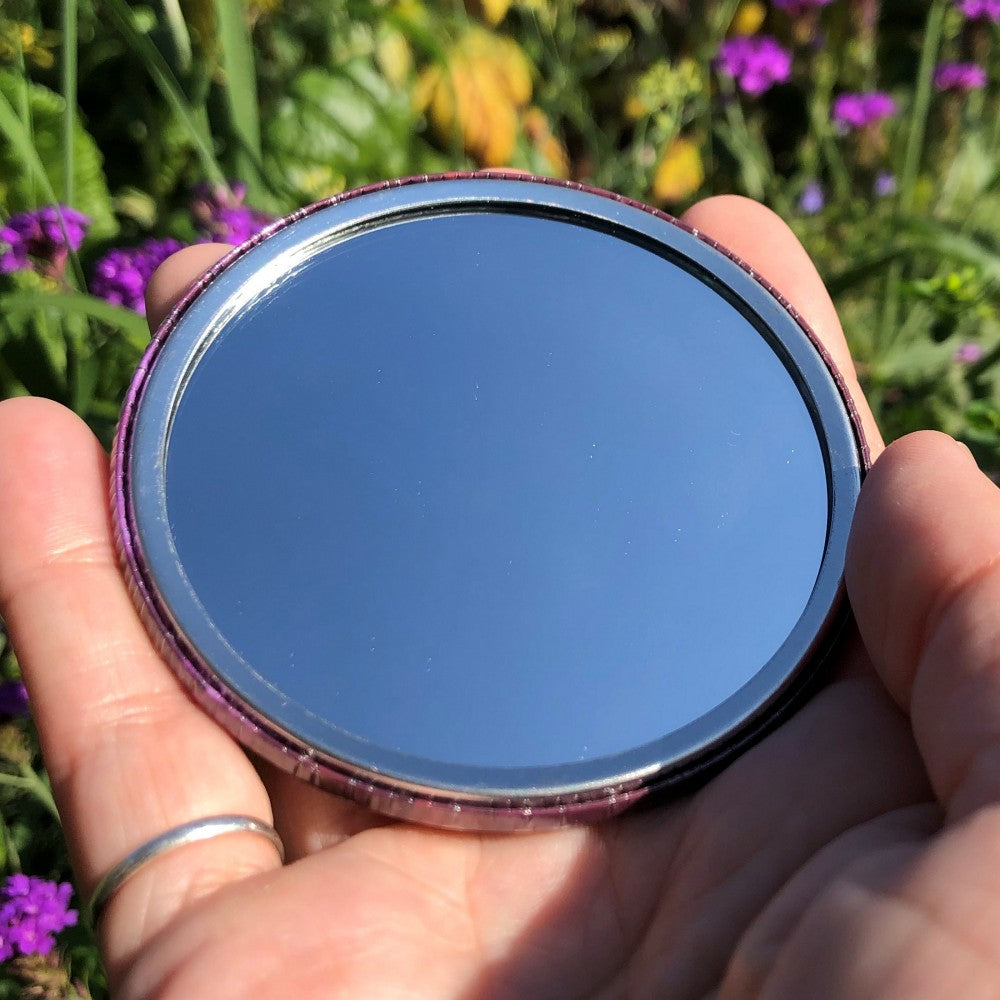 The mirrored side of the pocket mirror. The mirror fills the entire back, except for a small silver border.