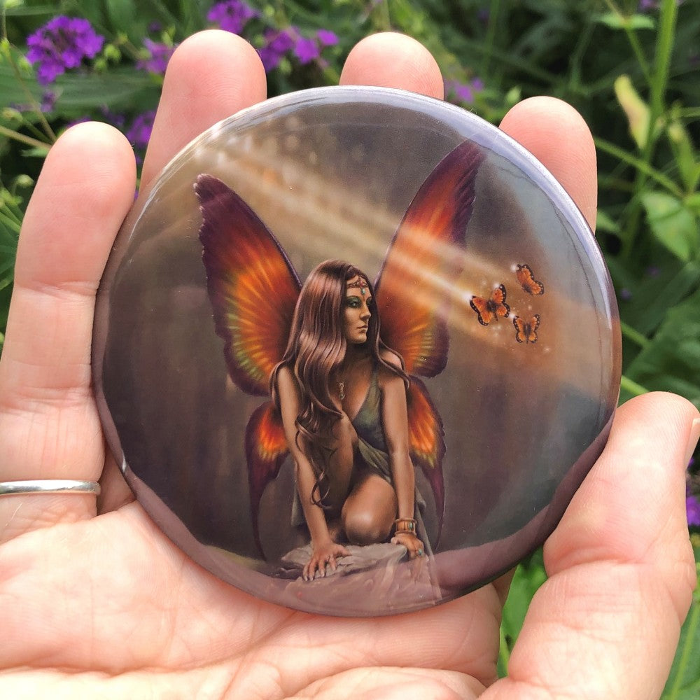 Painting of a fairy with long brown hair and wearing a green dress, crouched on a rock. The fairy has dark rainbow-coloured, butterfly shaped wings, and is looking sideways at three butterflies flying next to her.
