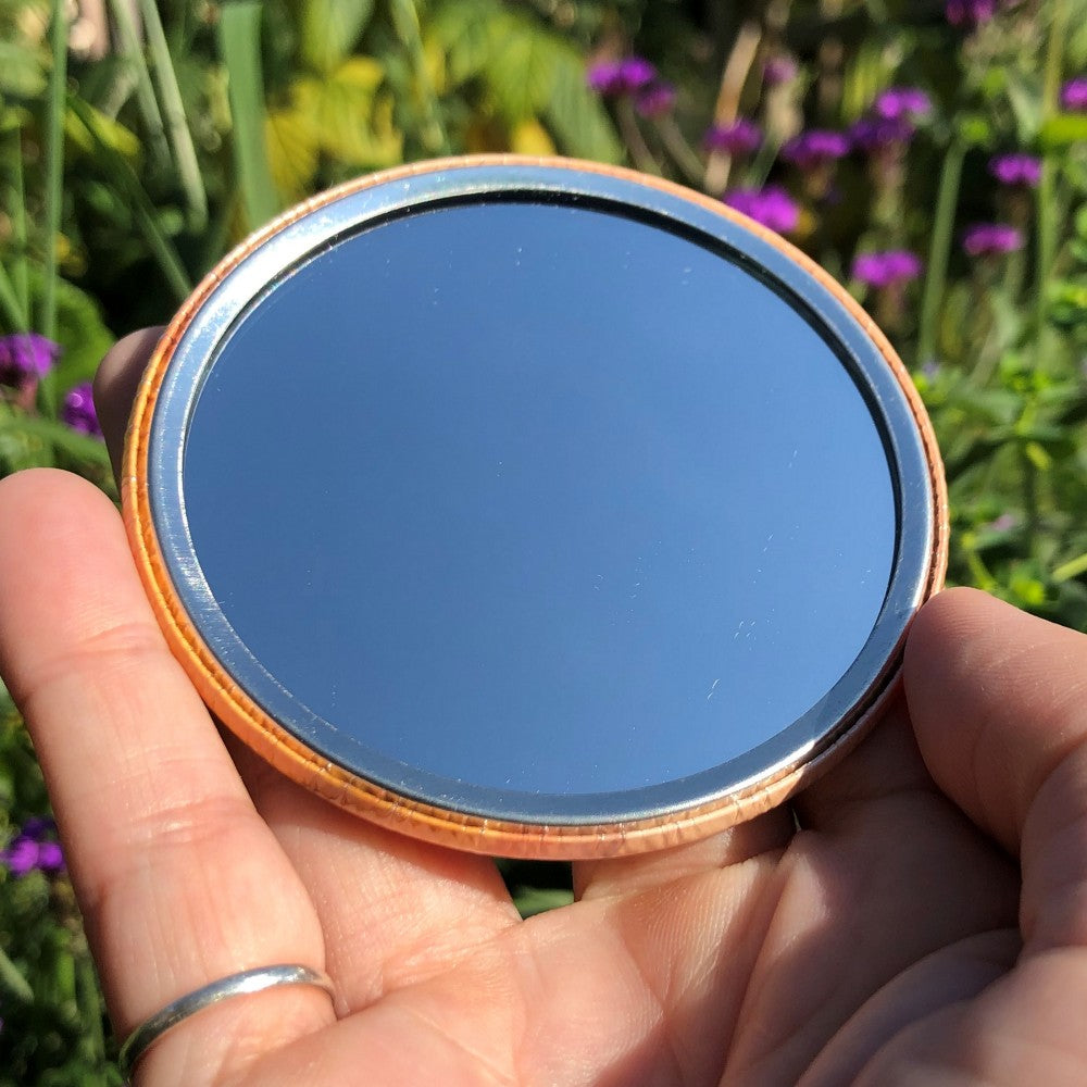 The mirrored side of the pocket mirror. The mirror fills the entire back, except for a small silver border.