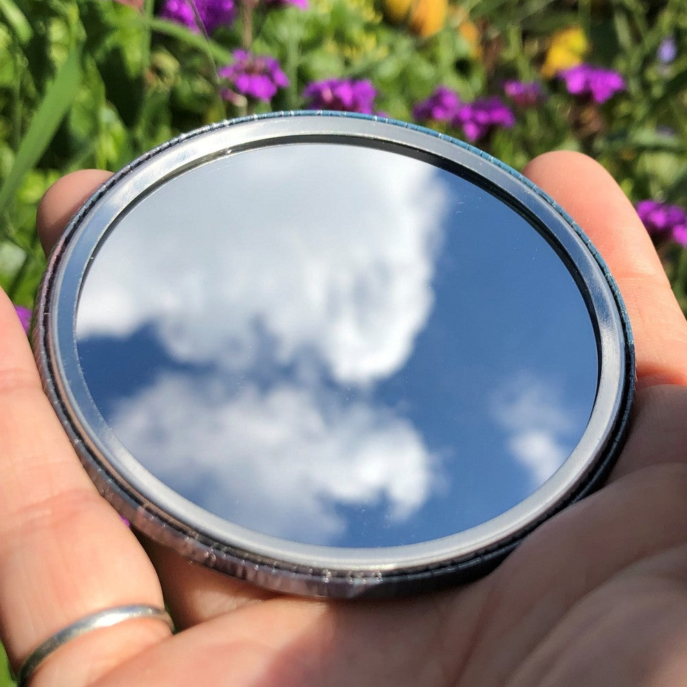The mirrored side of the pocket mirror. The mirror fills the entire back, except for a small silver border.