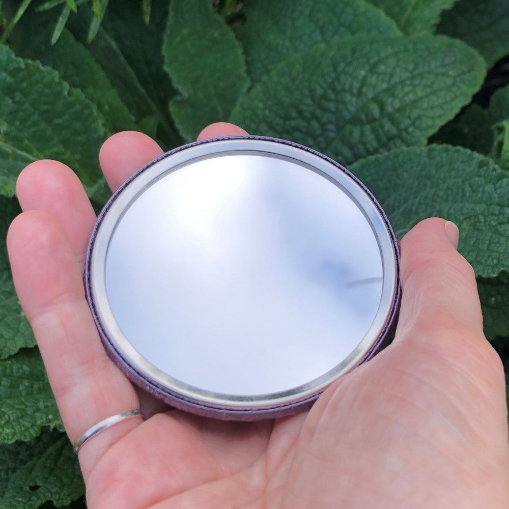 The mirrored side of the pocket mirror. The mirror fills the entire back, except for a small silver border.