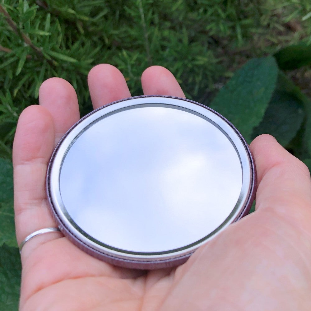 The mirrored side of the pocket mirror. The mirror fills the entire back, except for a small silver border.
