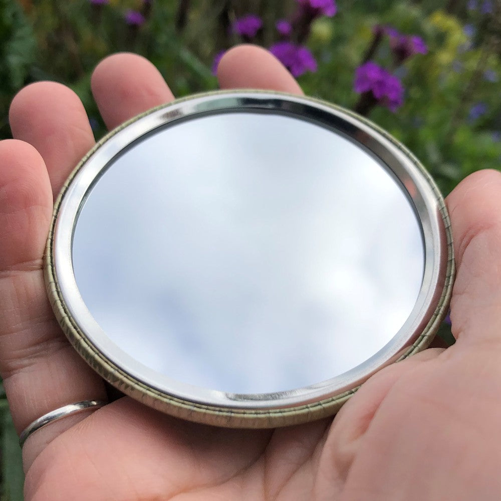 The mirrored side of the pocket mirror. The mirror fills the entire back, except for a small silver border.