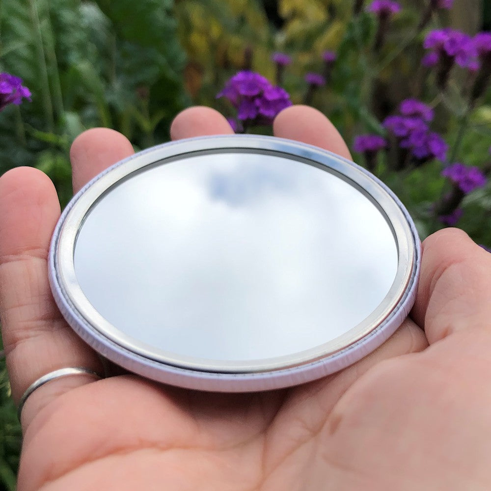 The mirrored side of the pocket mirror. The mirror fills the entire back, except for a small silver border.