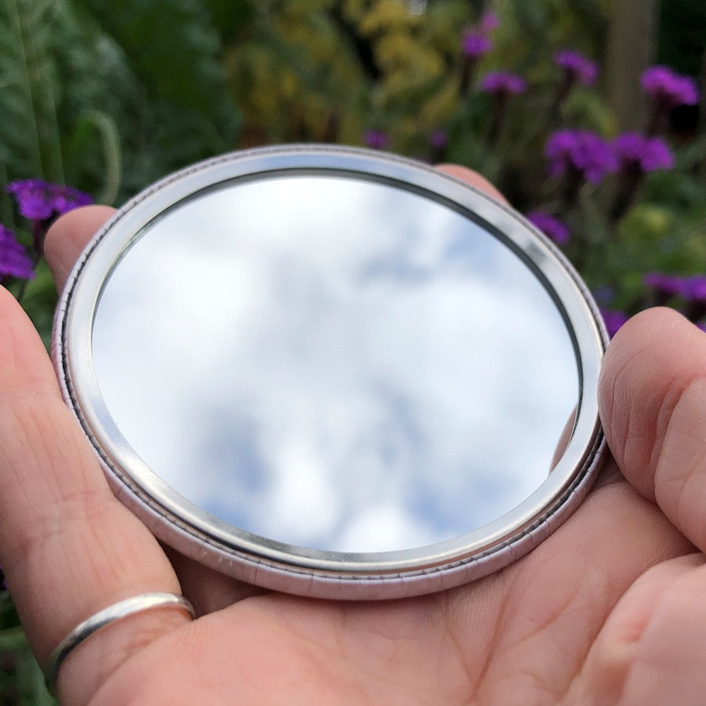 The mirrored side of the pocket mirror. The mirror fills the entire back, except for a small silver border.