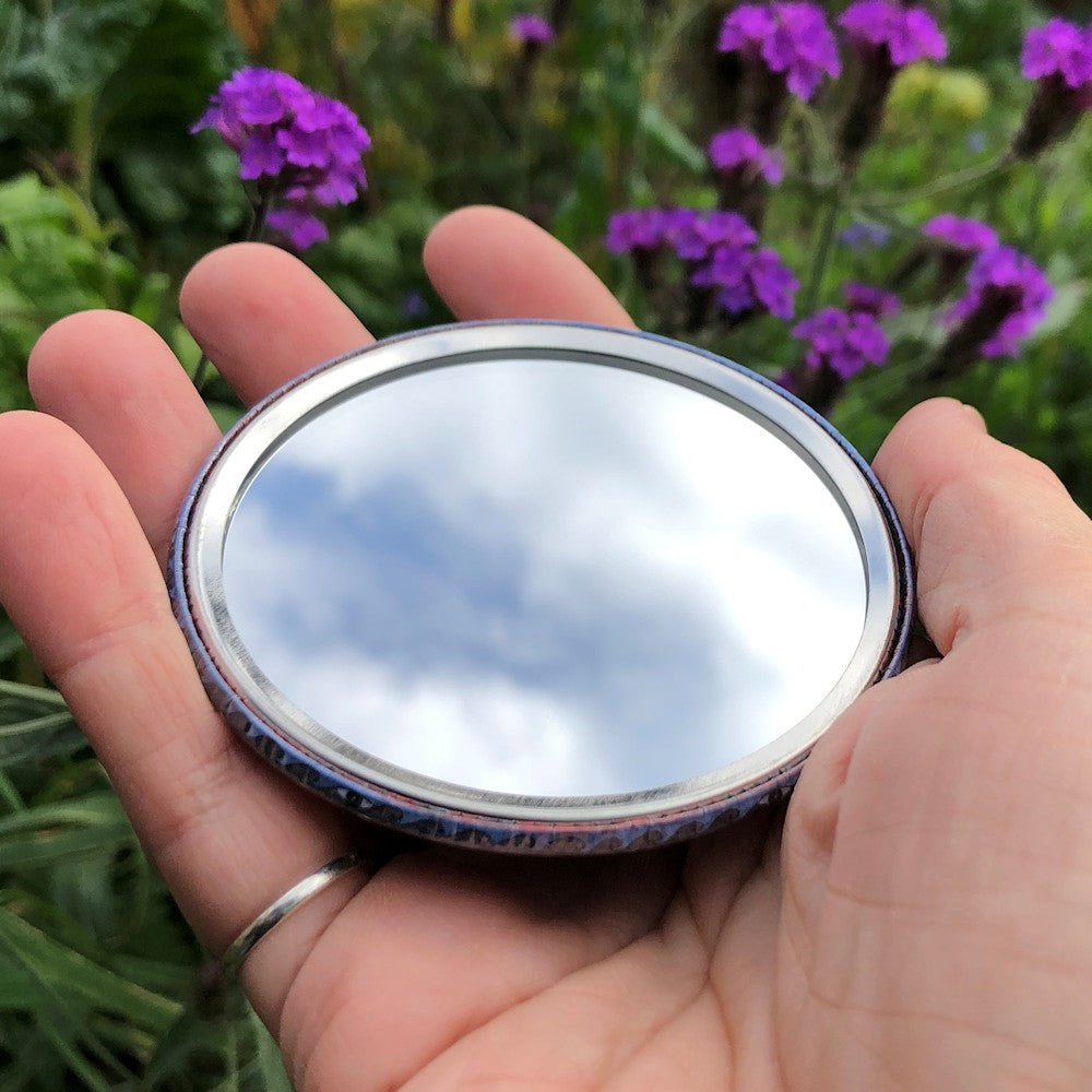 The mirrored side of the pocket mirror. The mirror fills the entire back, except for a small silver border.