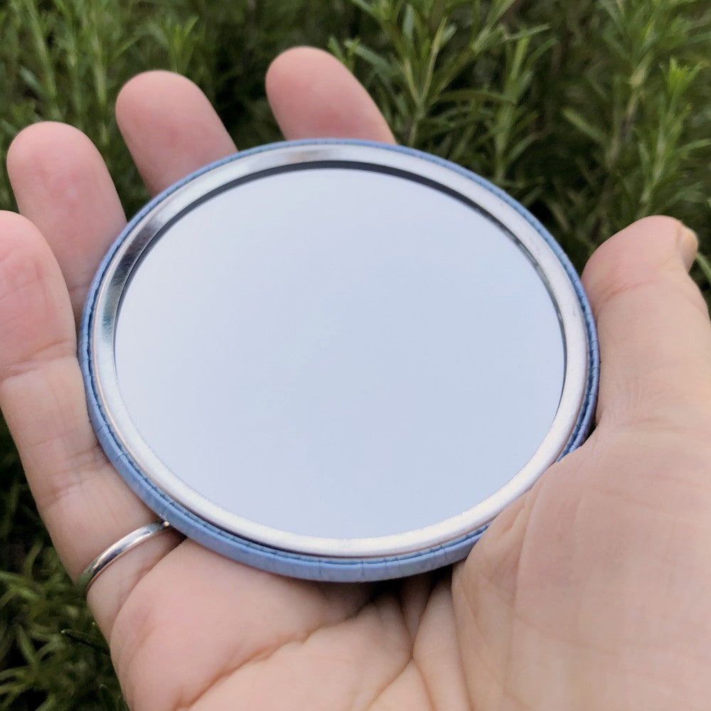 The mirrored side of the pocket mirror. The mirror fills the entire back, except for a small silver border.