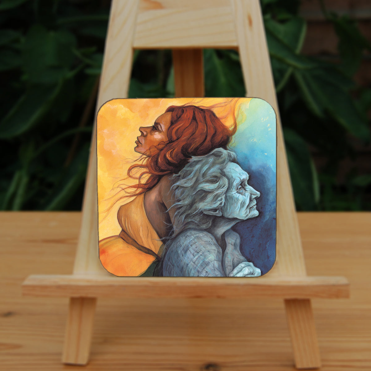 A square coaster: A painting of two diagonal halves: to the top/left, against a background of mottled orange, a young woman with red hair and orange dress faces to the left. She appears to be leaning against, and blending with, an elderly woman who faces towards the right/bottom in the other half of the design. This half is coloured in shades of blue and grey.
