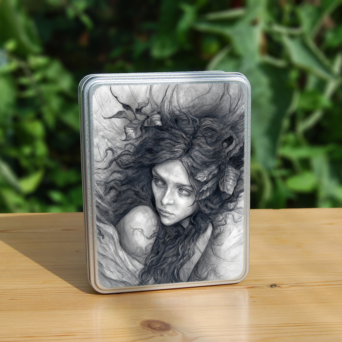 Rectangular metal tin: Pencil illustration of the head and shoulders of a young woman looking back over her shoulder. She has a mass of hair sticking out in all directions around her head and down her front. Leaves are woven - or perhaps stuck - in her hair.
