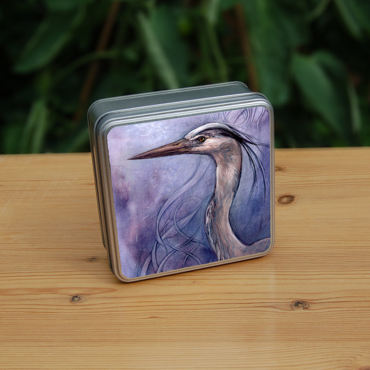 A square tin: A sideways view of the head and neck of a heron. The background is a mottled purple with a swirl pattern.