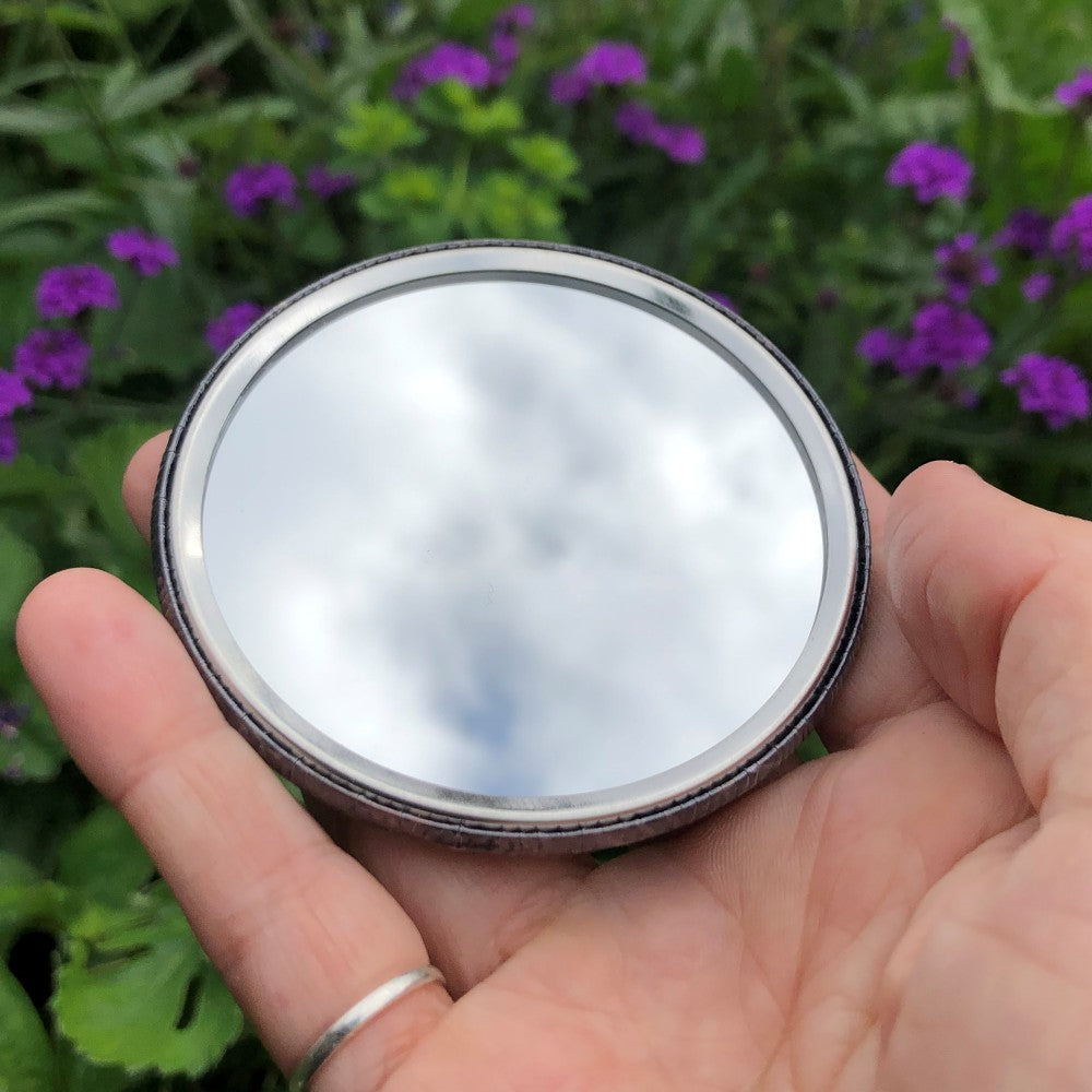 The mirrored side of the pocket mirror. The mirror fills the entire back, except for a small silver border.