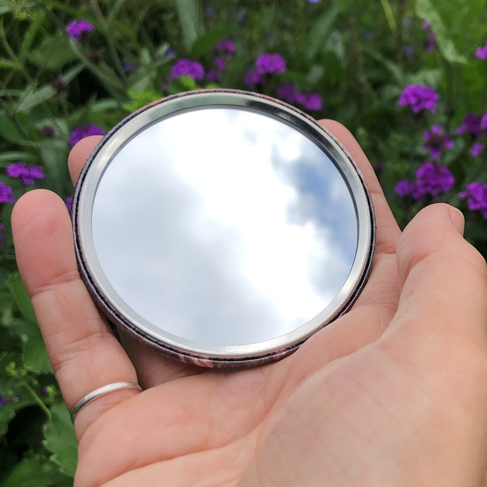 The mirrored side of the pocket mirror. The mirror fills the entire back, except for a small silver border.