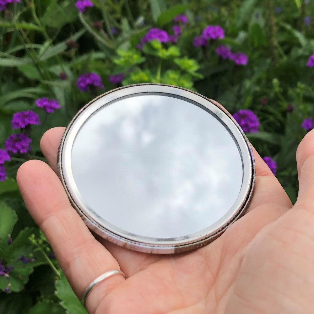 The mirrored side of the pocket mirror. The mirror fills the entire back, except for a small silver border.