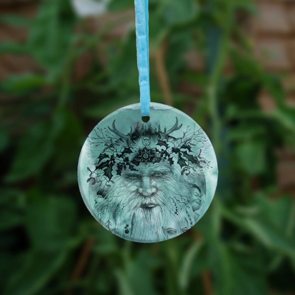 An outline pencil drawing of an old man with a beard facing the viewer. Small antlers sit above, and sprigs of holly surround the upper half of his face. Two small faces, facing outwards, appear from either side of his beard. A young elven face peers through bottom right. The design is colour-washed in green.