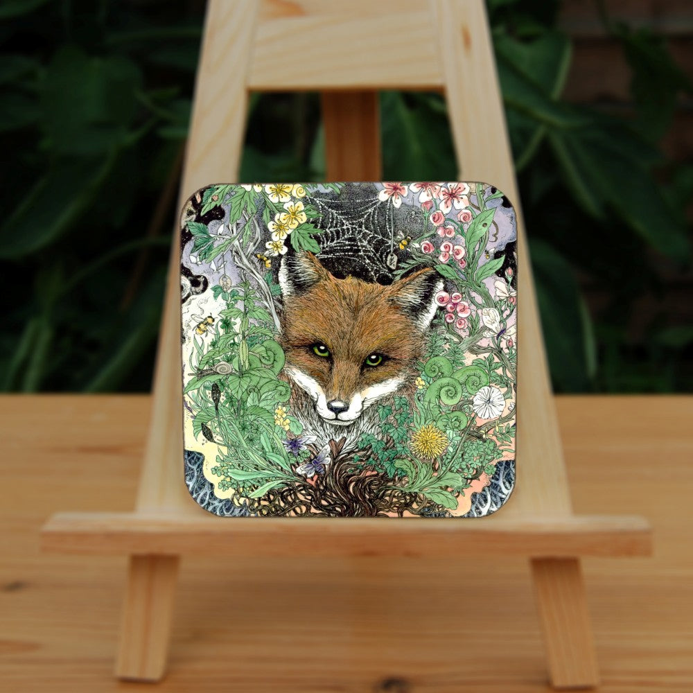 The head of a red fox looks towards the viewer. He's surrounded by a mass of leaves and flowers which rise out from a twisted tree trunk and tangled branches.