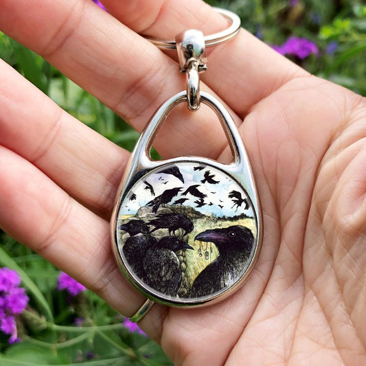 A large flock of ravens sit on and fly around a drystone wall surrounded by yellow-green grassy fields. The blue sky is broken with white clouds. In the foreground a raven holds a string of tokens in its beak, including a pentagram, key and Teiwaz rune.