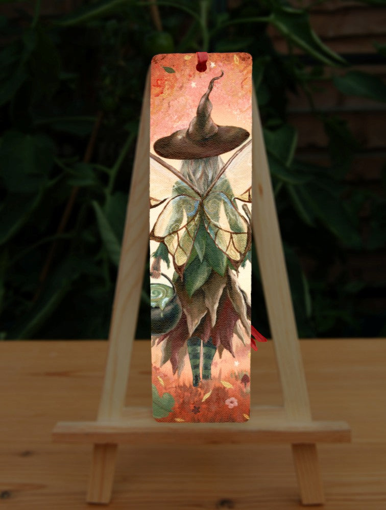 The rear view of a fairy walking in enchanted woodland. She has brown and white butterfly wings, and wears a pointed brown hat and green and brown dress. In her left hand she carries a cauldron. The woodland is cast in reds.