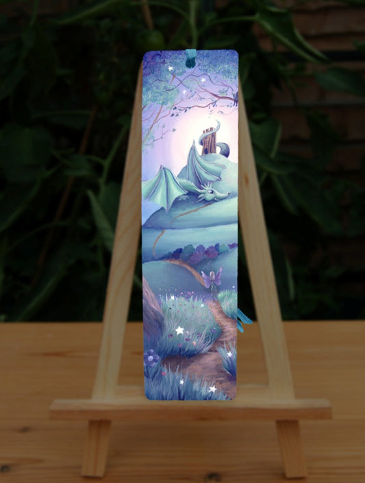 A winding path leads out from an enchanted forest. One fairy follows the path which leads up the side of a tall hill with steeply sloping sides. There's a tower on the top of the hill, and just below the tower, with its tail wound around it, sits a friendly dragon, wings partly open, and head resting on the path. There's a glow behind the top of the hill, fading to a blue night sky. Colours are rich teal, blue, purple and brown.