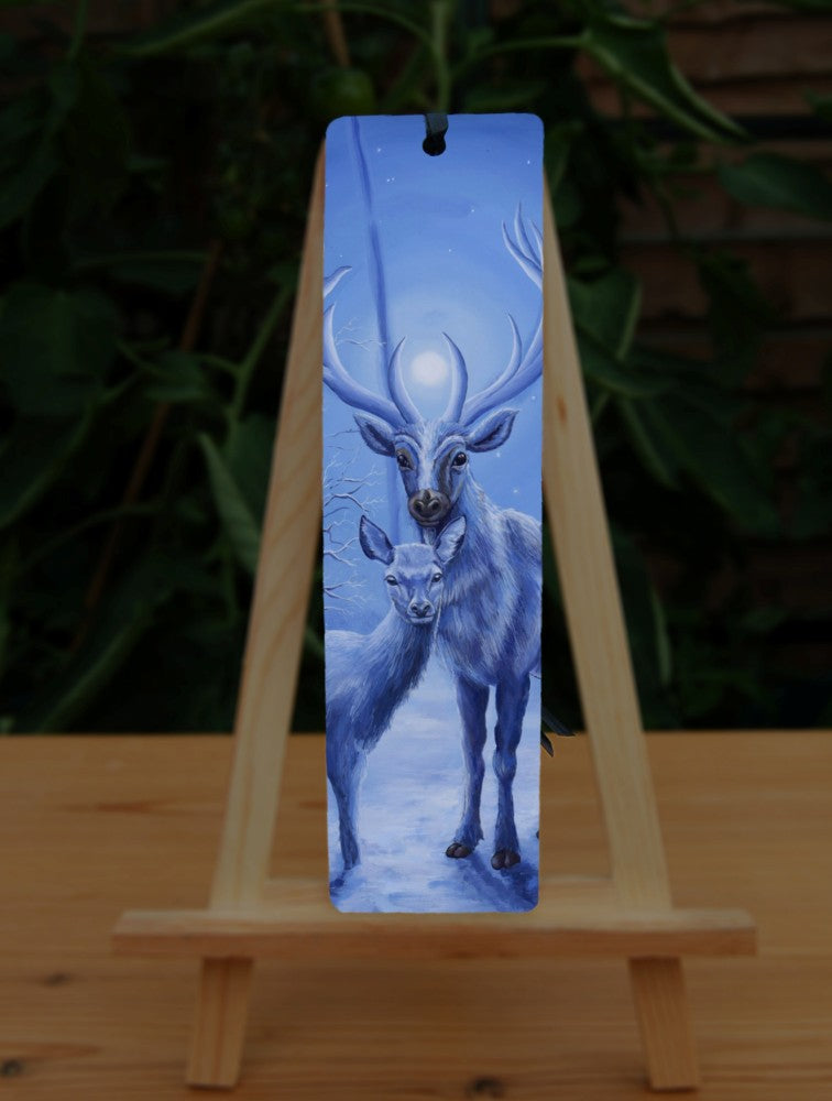 A stag and doe stand facing each other, heads turned towards the viewer. The design is cast in shades of blue. Snow lies underfoot. A wintery moon rises from between the stag's antlers, and stars can be seen in the sky beyond.