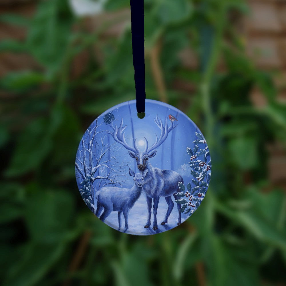 A stag and doe stand facing each other, heads turned towards the viewer. The design is cast in shades of blue. A robin perches on one of the stag's antlers. Snow lies underfoot, and on the branches of the berried holly tree to the right, and bare tree to the left. A wintery moon rises from between the stag's antlers, and stars can be seen in the sky beyond.