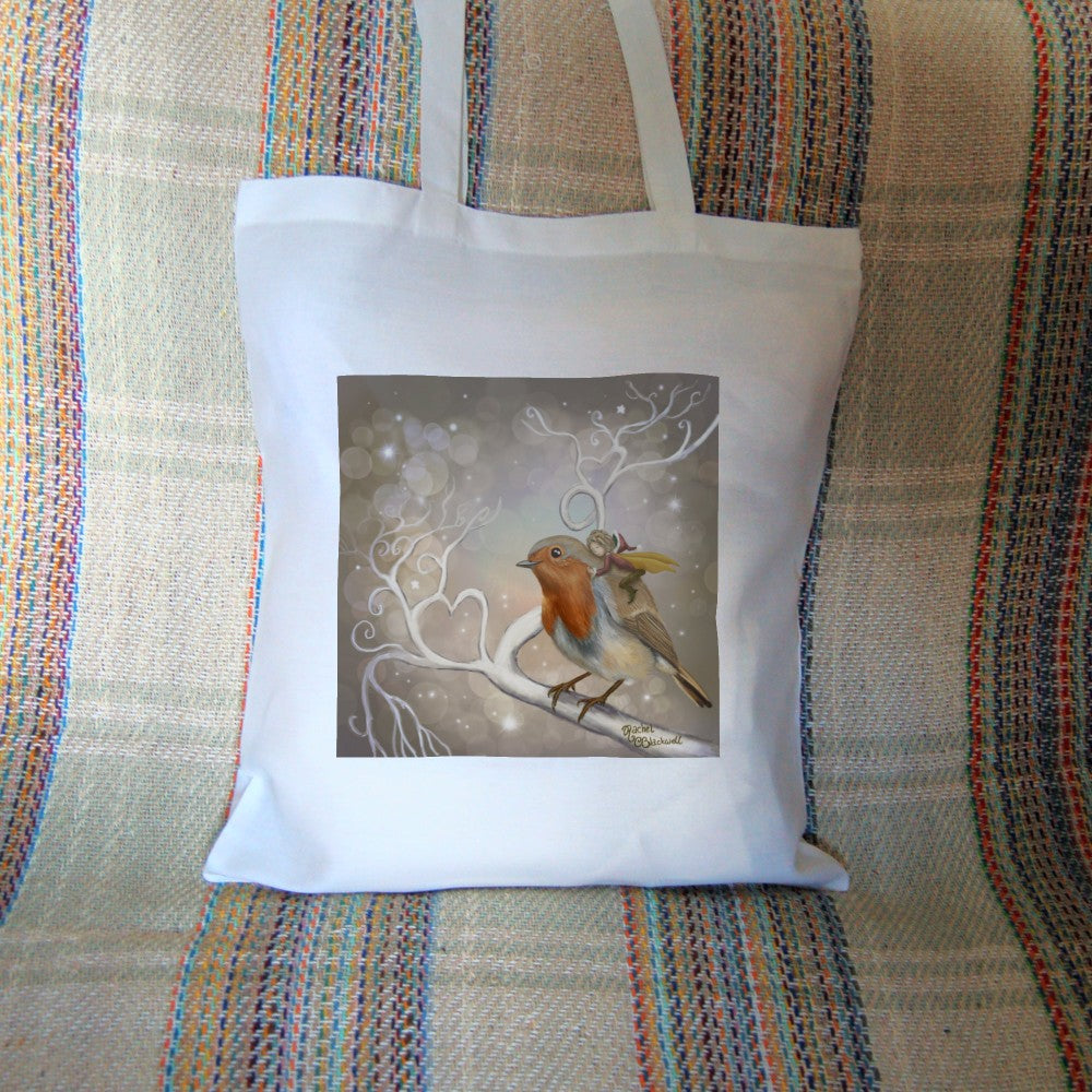 A robin perches on a white leafless branch. Twigs twist and curl from the branch, one forming a heart shape. A fairy with mustard-coloured wings and wearing red and brown, and a santa hat, holds onto the back of the robin, eyes closed and looking content. The background is mid-brown with stars and bubbles.