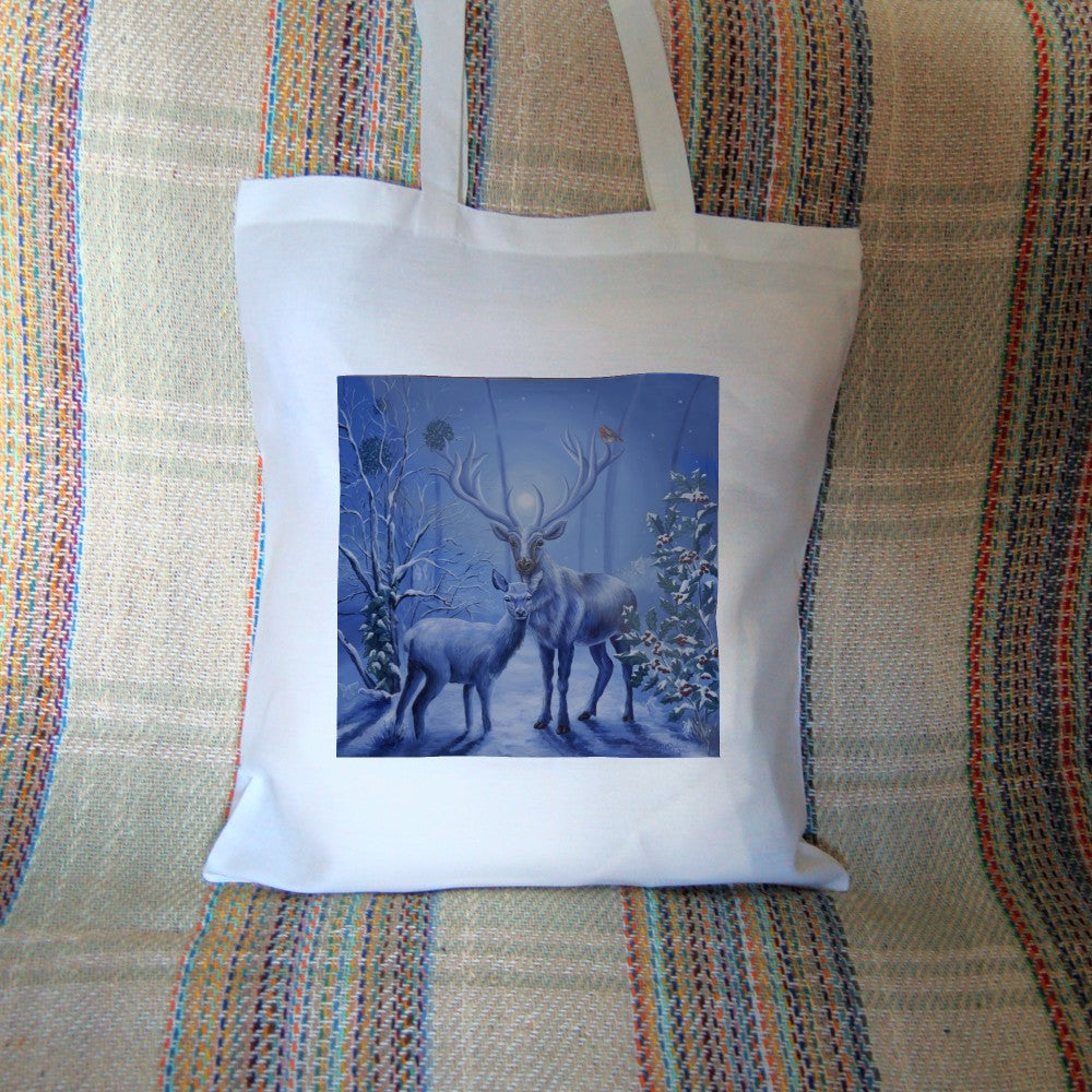 A stag and doe stand facing each other, heads turned towards the viewer. The design is cast in shades of blue. A robin perches on one of the stag's antlers. Snow lies underfoot, and on the branches of the berried holly tree to the right, and bare tree to the left. Pale fairies flit through the branches. Balls of mistletoe sit in the bare tree. A wintery moon rises from between the stag's antlers, and stars can be seen in the sky beyond.