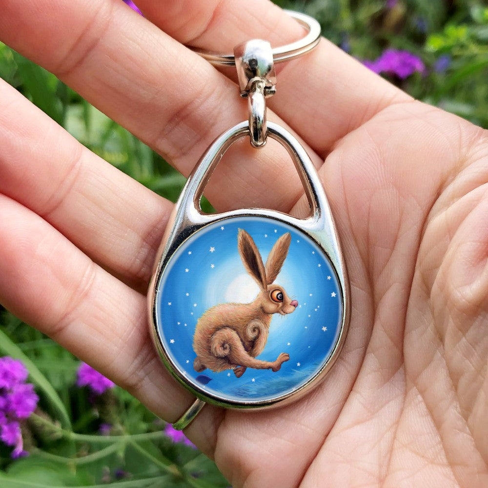 A cartoon-like hare with huge orange eyes, pink nose and brown shaggy fur dashes across the design from left to right. He's running so fast that his front legs reach under his back legs, and his back legs reach in front of his front legs. Behind him, stars shine around a glowing halo of white, fading to blue away from the centre.