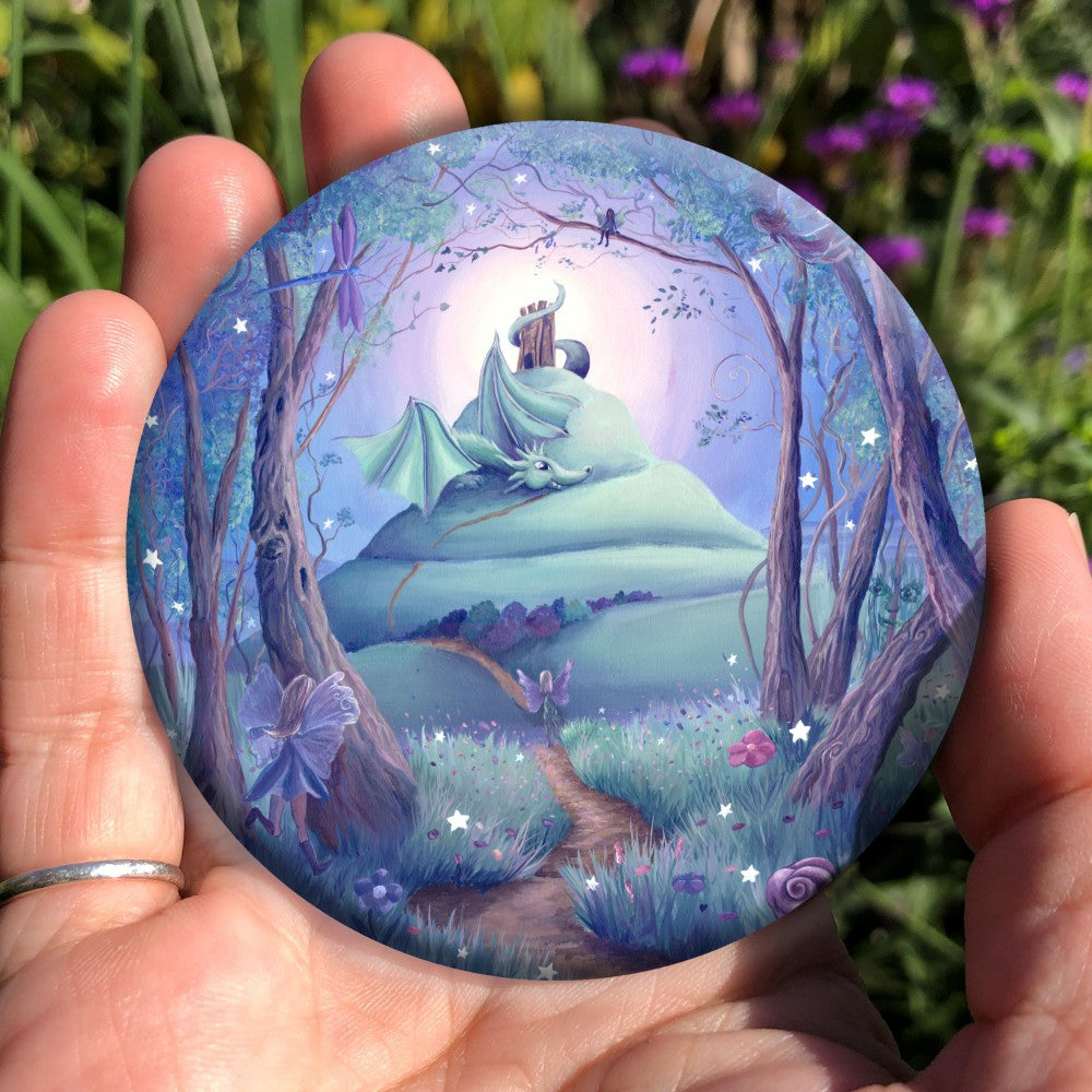 A winding path leads out from an enchanted forest where many fairies, and a dragonfly, can be seen. One fairy follows the path which leads up the side of a tall hill with steeply sloping sides. There's a tower on the top of the hill, and just below the tower, with its tail wound around it, sits a friendly dragon, wings partly open, and head resting on the path. There's a glow behind the top of the hill, fading to a blue night sky. Colours are rich teal, blue, purple and brown.