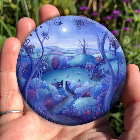 A path out of woodland leads away down a slope towards an open gate. Beyond the gate, sheep graze in a field, and beyond that there's a steep hill with a large dead tree on top. A patchwork of fields can be seen in the distance. A full moon shines in a mid-blue, starlit sky. The design is very colourful, with teal, purple, pink and blue hedges, trees, and fields.