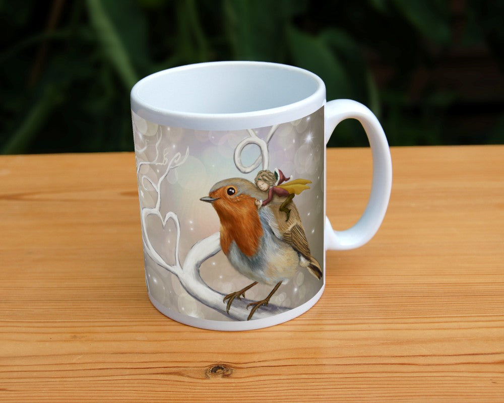 A robin perches on a white leafless branch. Twigs twist and curl from the branch, one forming a heart shape. A fairy with mustard-coloured wings and wearing red and brown, and a santa hat, holds onto the back of the robin, eyes closed and looking content. The background is mid-brown with stars and bubbles.
