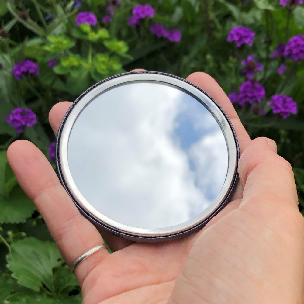 The mirrored side of the pocket mirror. The mirror fills the entire back, except for a small silver border.