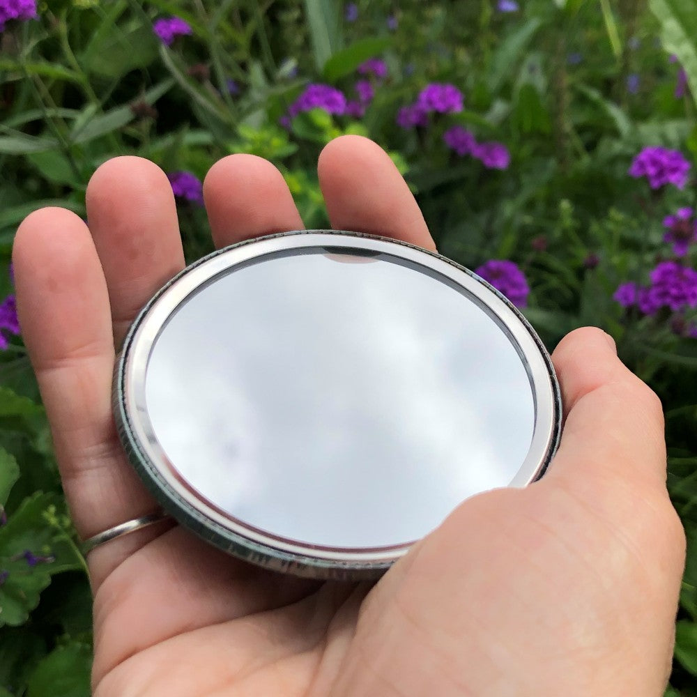 The mirrored side of the pocket mirror. The mirror fills the entire back, except for a small silver border.