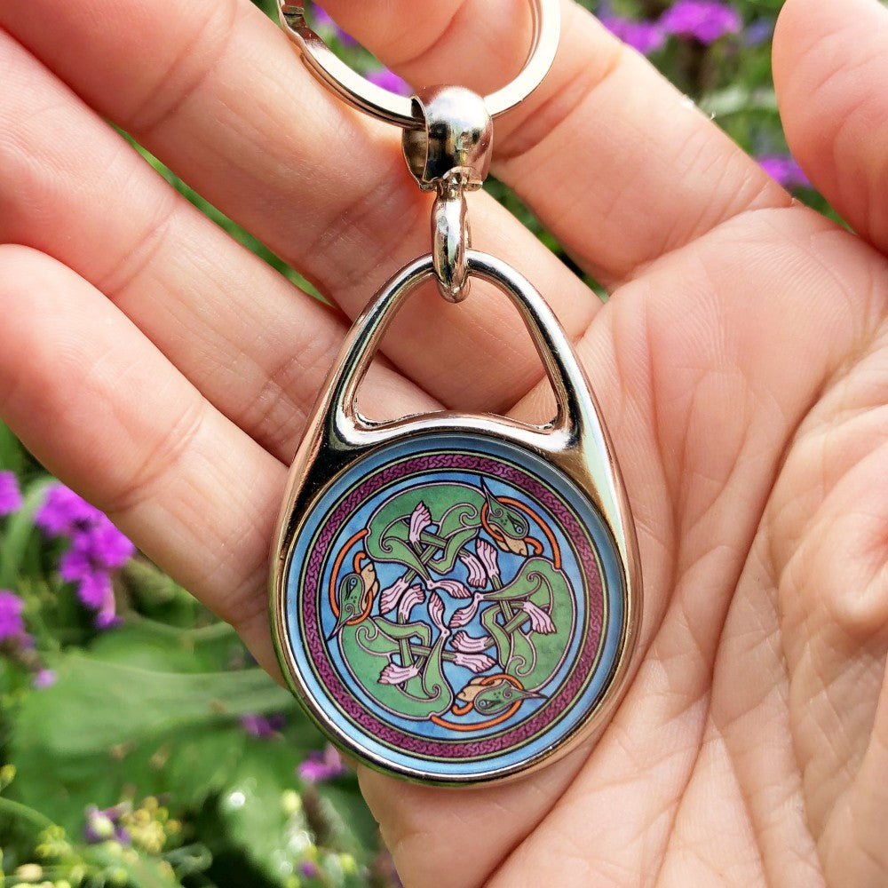 Three entwined Celtic-style dogs in a circle. The dogs are green with pink feet and orange tails. Each dog has the tail of the next dog in its mouth. Enclosed in a ring of dark red Celtic knotwork. The background is mid-blue.