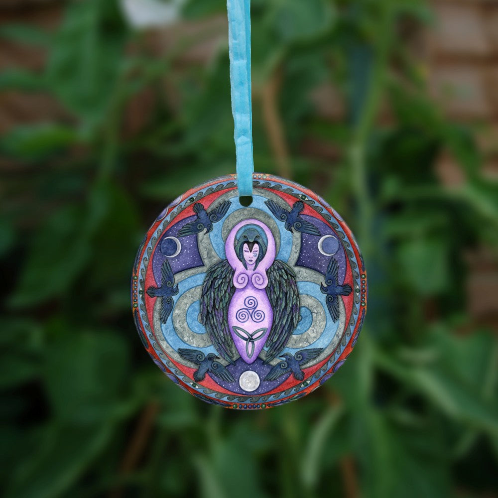 A raven stands behind a purple Goddess figure, its huge wings folded down her sides. She stands in the centre of a ring. Ravens fly around the inside of the ring, with each aspect of the triple moon also present. Colours are purple, red, and blue.