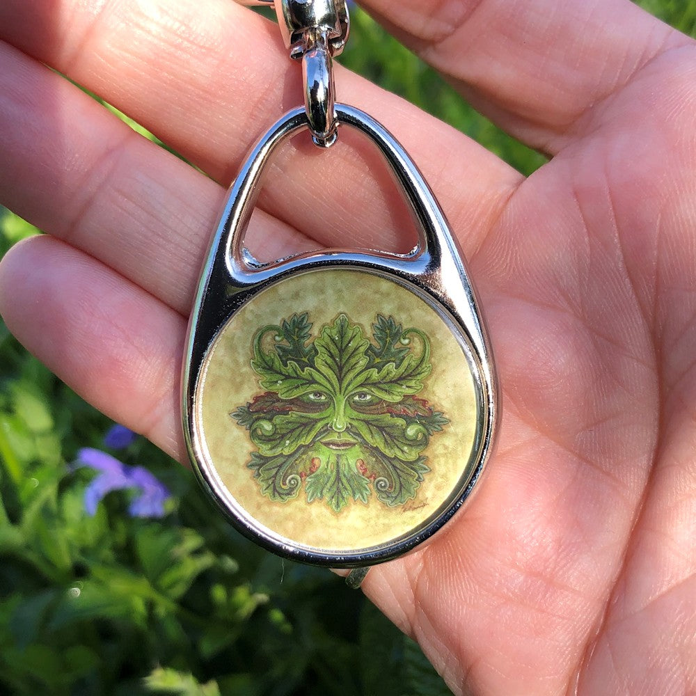 A Green Man. Green oak leaves grow out from around his eyes, nose and mouth. Some leaves have red edges. The background is a mottled pale green.