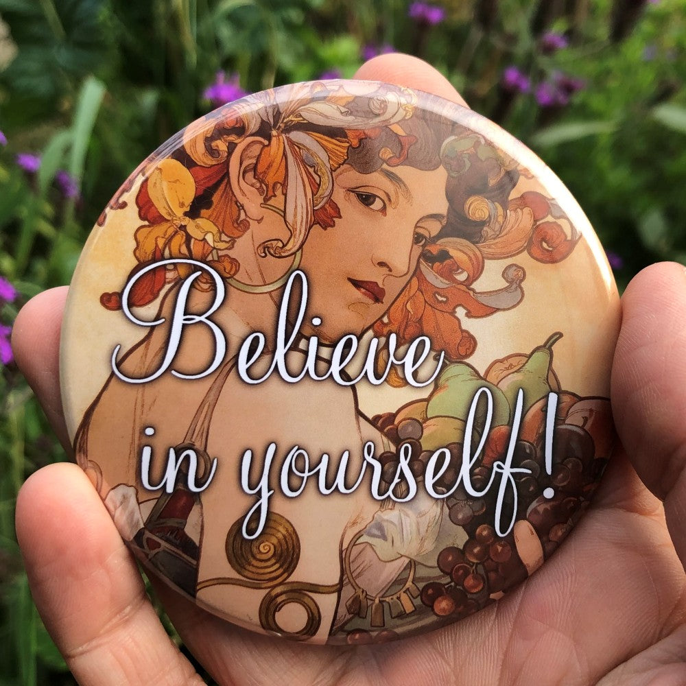 Art Nouveau style image of a young woman with dried flower petals in her hair. She is partially turned away from the viewer, and looking back over her shoulder. She wears a strappy dress and is carrying a selection of fruit. Colours are orange, brown and cream. "Believe in yourself!" is written in decorative white text over the centre of the design.