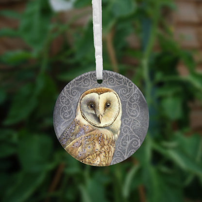Circular hanging ornament with a white ribbon: A pale brown bird with cream face sits sideways, coming in from the left hand side of the design, and looking directly at the viewer. The background is grey, overlaid a paler grey border consisting of a pattern of swirls.
