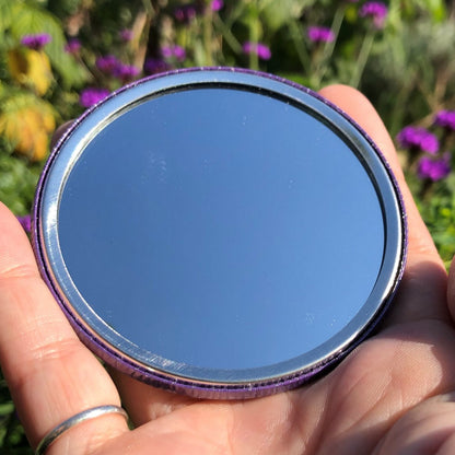 The mirrored side of the pocket mirror. The mirror fills the entire back, except for a small silver border.