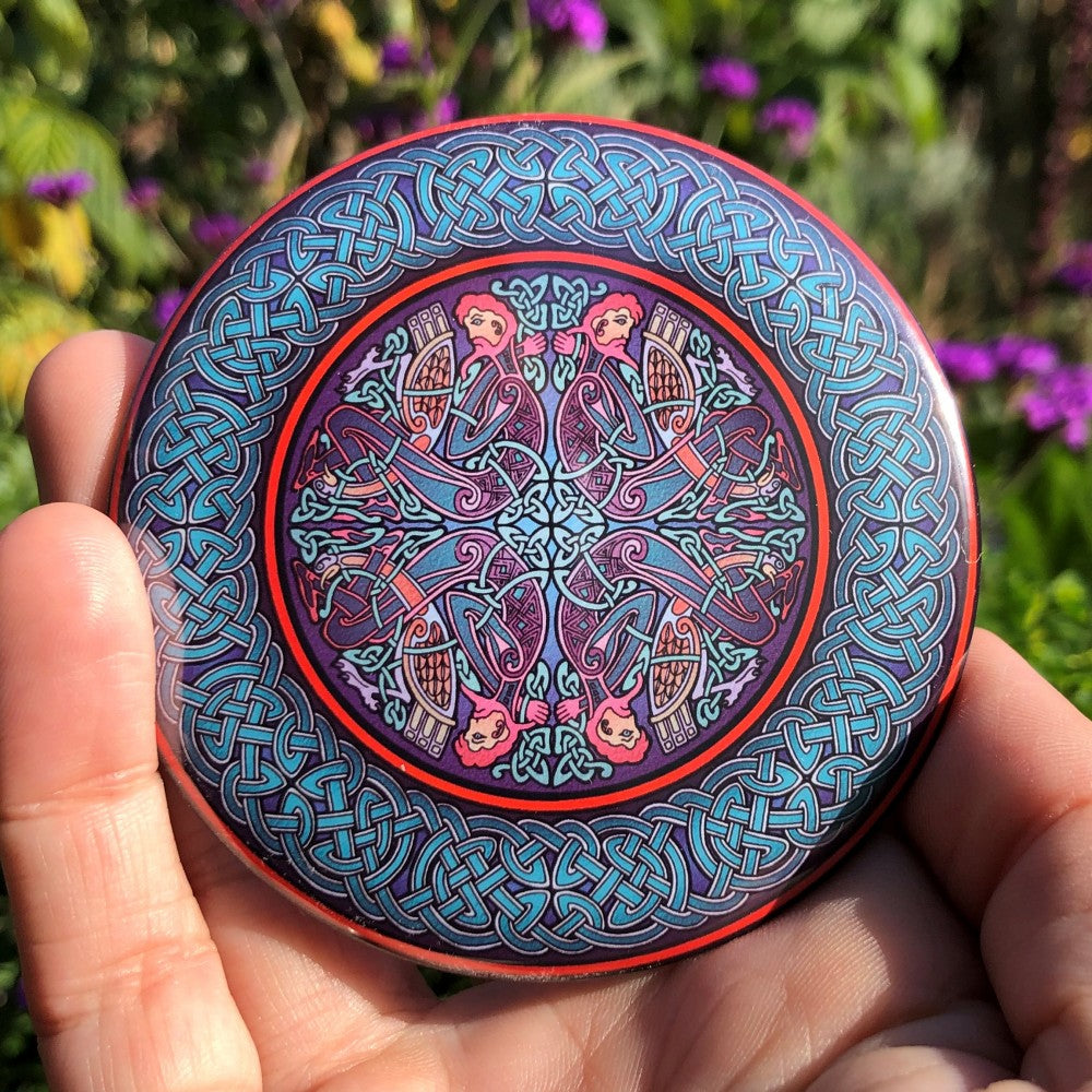 A circular Celtic design featuring four men and four birds facing left and right, then the same but upside down, sits in the centre of the design. Colours are blues, reds, pinks and purples. A wide Celtic knot border in shades of blue with a red edge surrounds the central design.