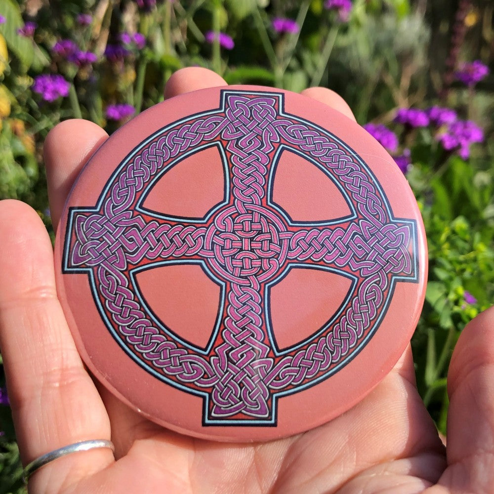 A Celtic cross design. Traditional Celtic knotwork is in the centre of the cross. The background is a plain orange/peach colour. The Celtic design is black, pale blue, and purple fading to pink in the centre.