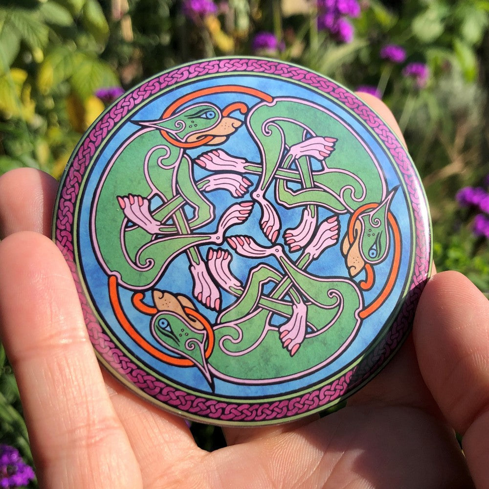Three entwined Celtic-style dogs in a circle. The dogs are green with pink feet and orange tails. Each dog has the tail of the next dog in its mouth. Enclosed in a ring of dark red Celtic knotwork. The background is mid-blue.