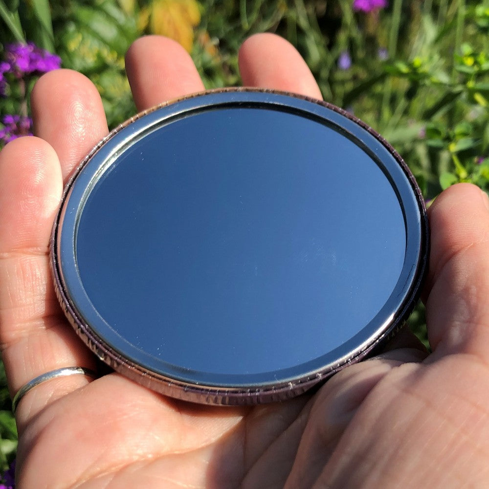 The mirrored side of the pocket mirror. The mirror fills the entire back, except for a small silver border.