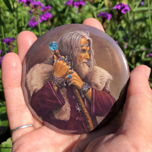 A man with long grey hair and a beard leans on his staff, looking intently to the right. He is wearing a deep purple coat with a pale-coloured fur mantle, and many silver bracelets and rings. A silver pentagram can be glimpsed from behind his staff. The top of the wooden staff has a large, turquoise jewel at the top.