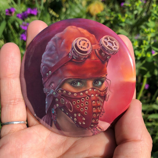 The head of a woman wearing a red leather fitted hood and studded face mask covers all of her face except her eyes, which look towards the viewer. She also wears a red leather and bead necklace, and steampunk-style googles, lifted up onto her forehead. The background is shades of red with a brighter yellow flash.